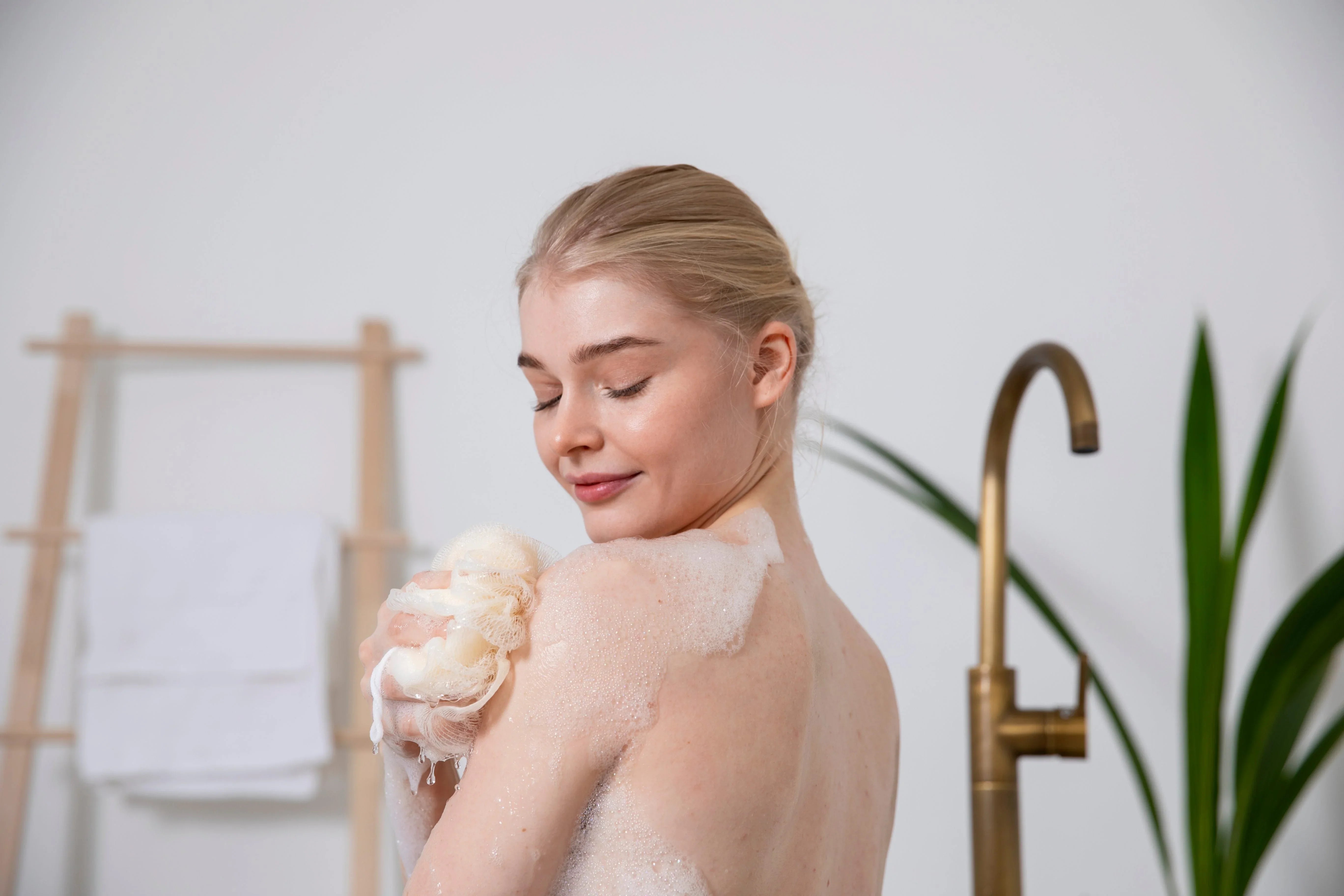 Woman enjoying bubble bath with loofah sponge in modern bathroom, spa self-care