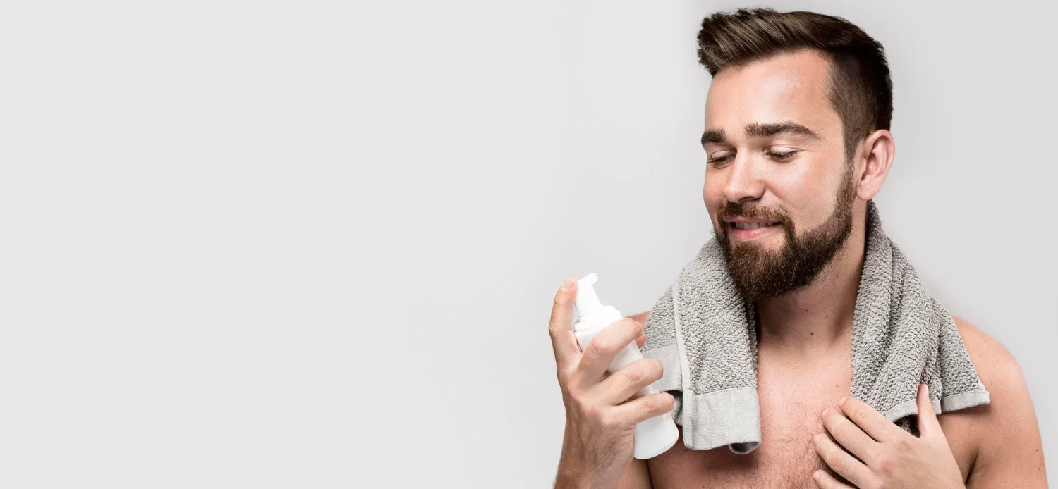 Bearded man with towel holding skincare bottle for men's grooming on light background