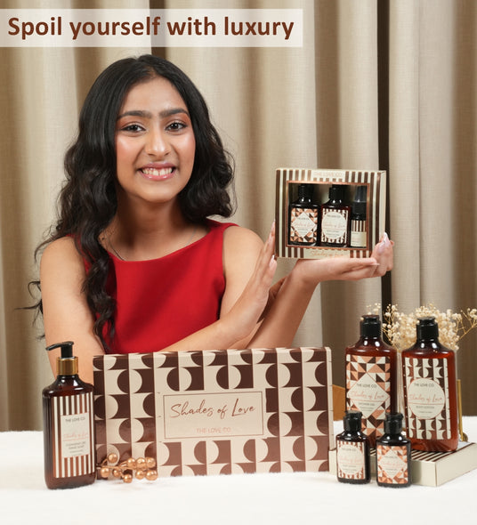 Smiling woman in red dress holding The Love Co. Shades of Love gift set, with more products displayed in front.