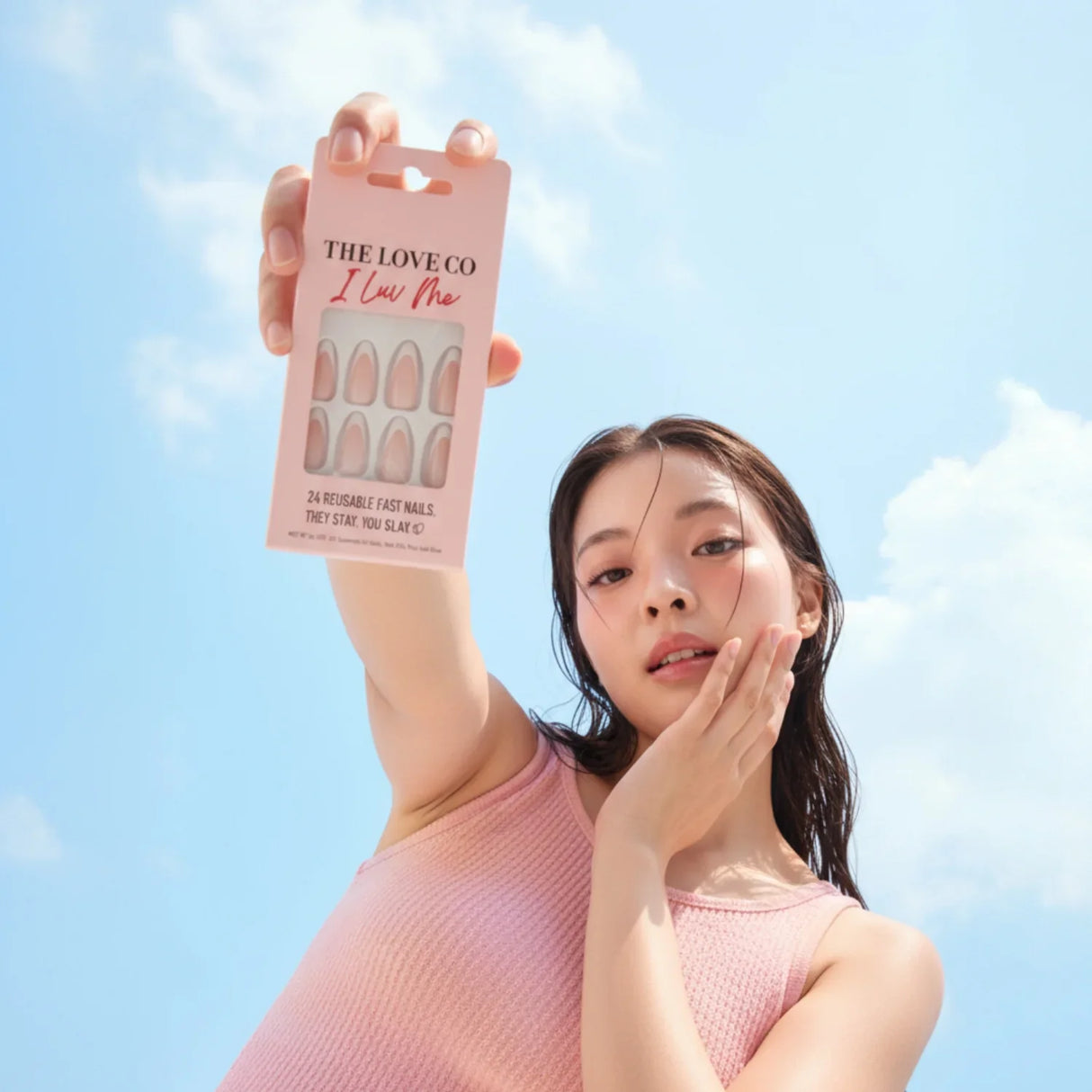 Woman in pink tank top holding The Love Co reusable press on nails against blue sky