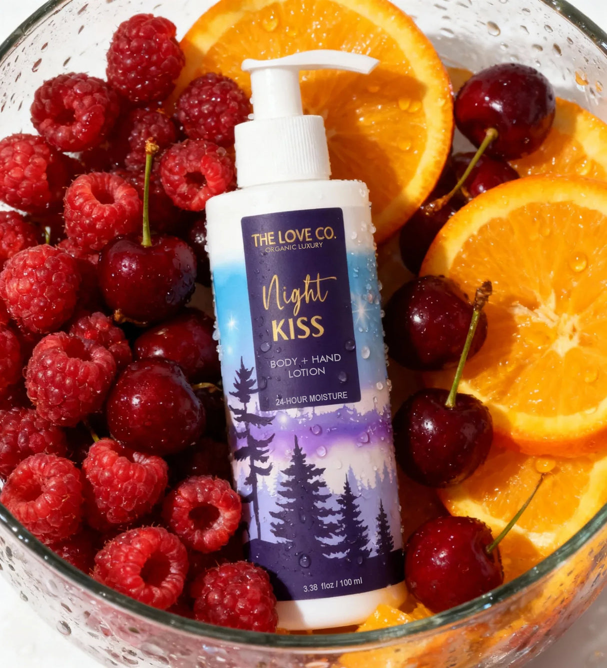 The Love Co Night Kiss body and hand lotion bottle in bowl with raspberries, cherries, oranges