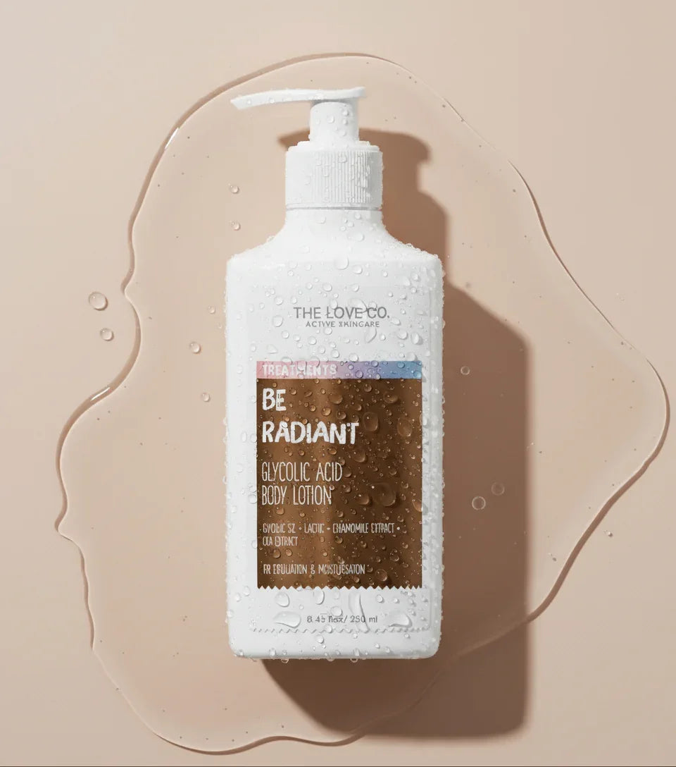 The Love Co. Be Radiant Glycolic Acid Body Lotion bottle with water droplets on a beige background.