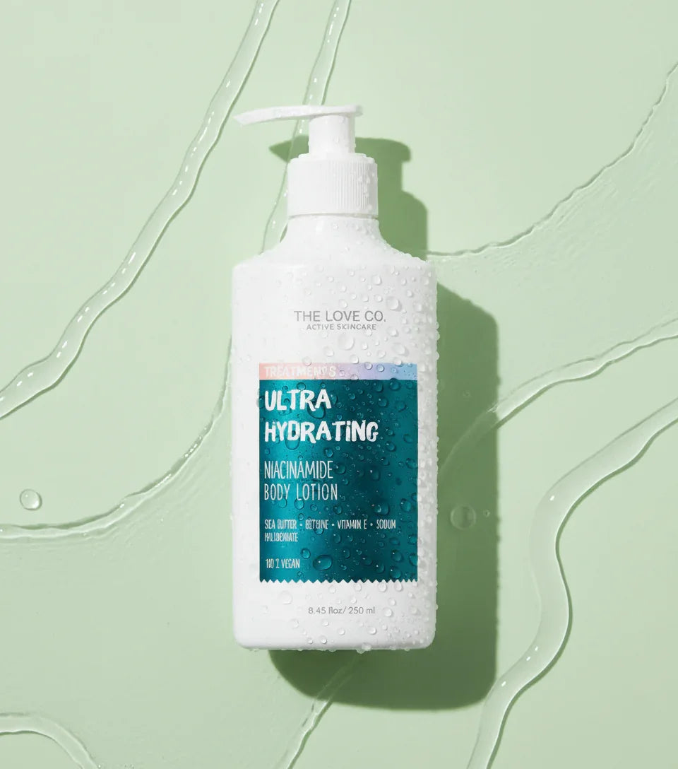 The Love Co Ultra Hydrating Niacinamide Body Lotion bottle with water drops on light green background