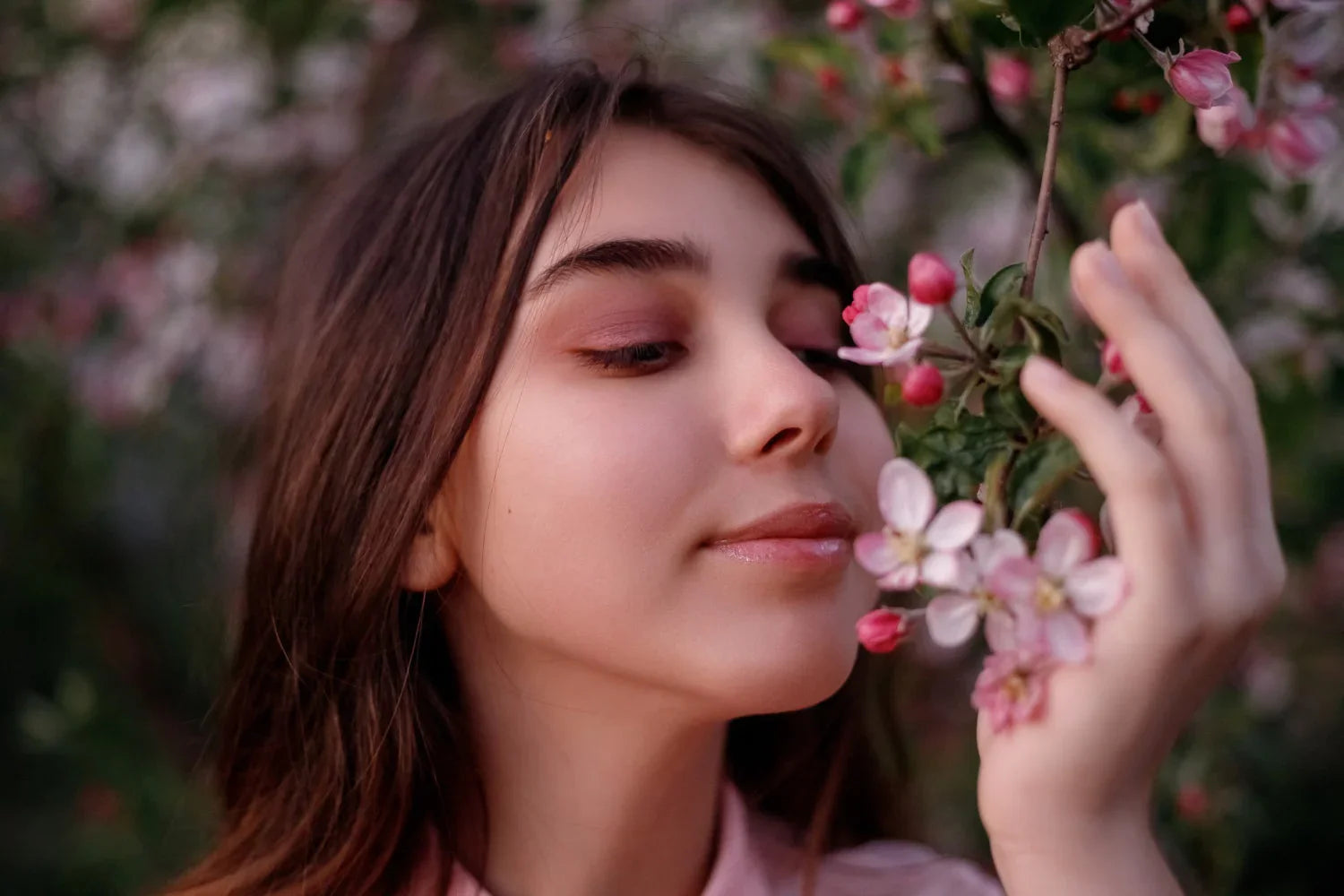 Young woman with natural makeup smelling pink apple blossoms outdoors