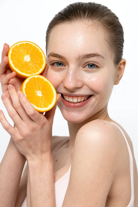Smiling woman with glowing skin holding fresh orange halves, Vitamin C skincare concept