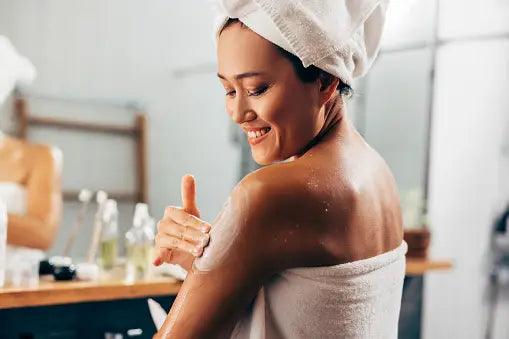 Smiling woman applying in-shower moisturizer on shoulder, bathroom skincare routine