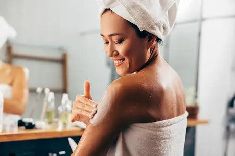 Smiling woman applying in-shower moisturizer on shoulder, bathroom skincare routine