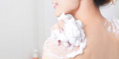 Woman using foaming body wash in shower, close up on back and shoulder