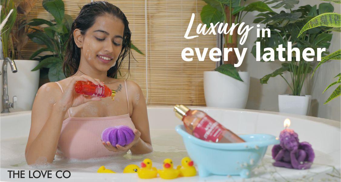 Woman using The Love Co body wash in a luxurious bathtub with plants and rubber ducks