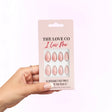 Hand holding The Love Co I Luv Me reusable pink press-on nails pack against light background