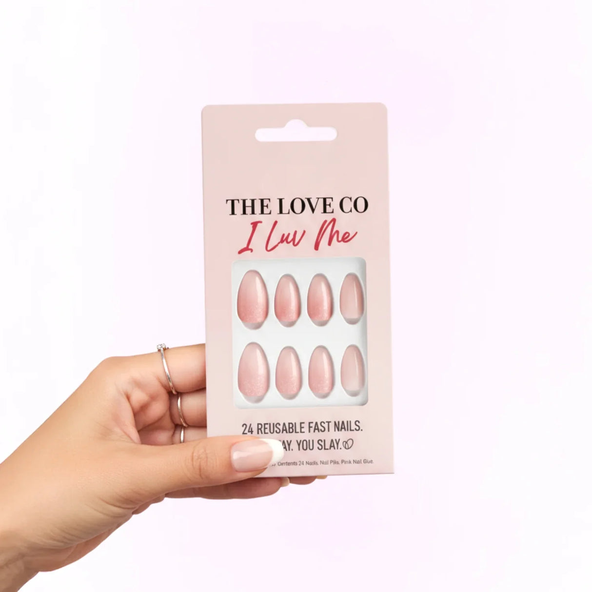 Hand holding The Love Co I Luv Me reusable pink press-on nails pack against light background
