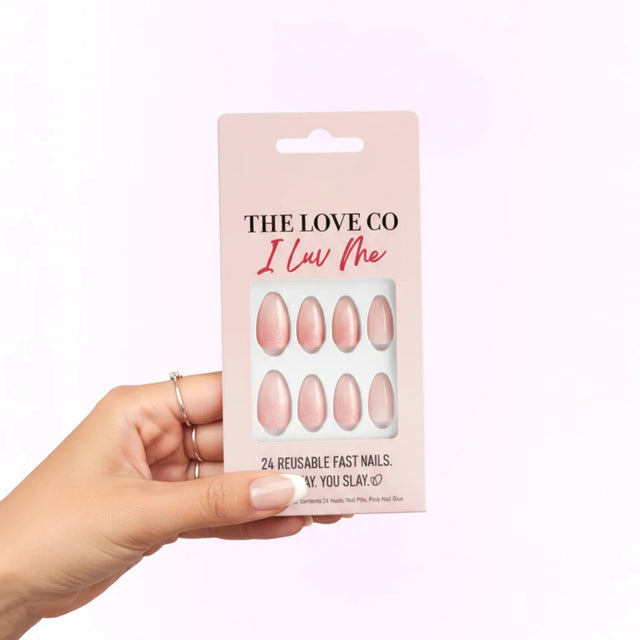 Hand holding The Love Co I Luv Me reusable pink press-on nails pack against light background