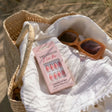Reusable pink press on nails box and brown sunglasses in a woven beach bag on white fabric