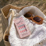 Reusable pink press on nails box and brown sunglasses in a woven beach bag on white fabric