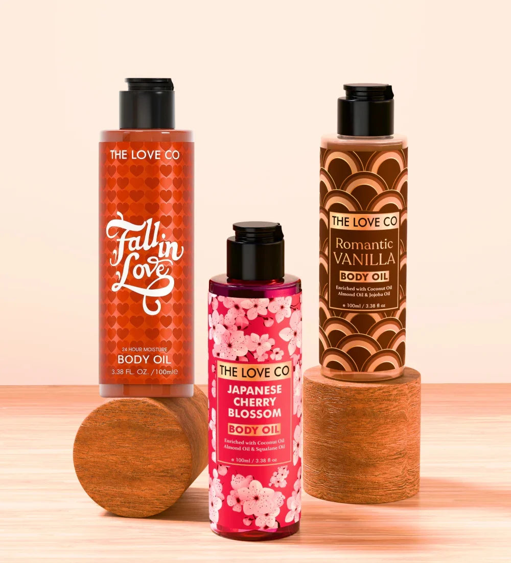 The Love Co body oils—Fall in Love, Japanese Cherry Blossom, Romantic Vanilla—on wooden stands