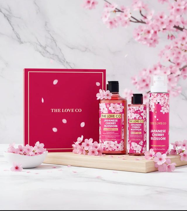 The Love Co Japanese Cherry Blossom gift set with shower gel, body oil, and mist, surrounded by pink cherry blossoms on marble background.