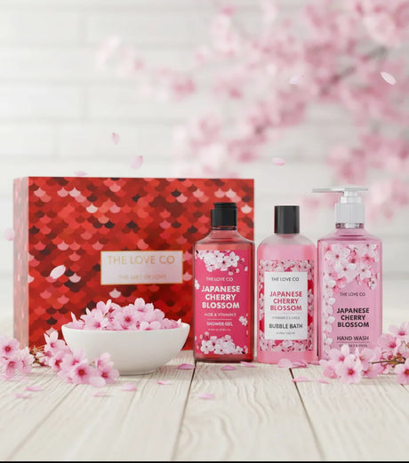 The Love Co Japanese Cherry Blossom gift box with shower gel, bubble bath, and hand wash set, surrounded by pink cherry blossoms.