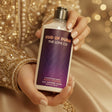 Hand holding a bottle of 'Oud of Dubai' body lotion with a blurred gold and purple background.