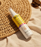 Sunscreen spray bottle with yellow label on a woven mat and beige fabric background