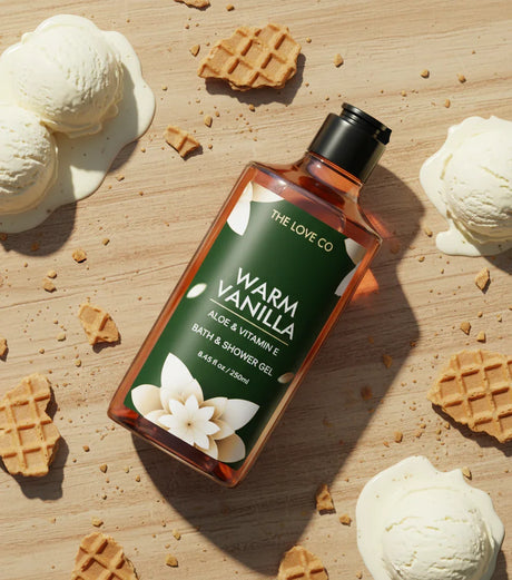 Bottle of 'Warm Vanilla' bath and shower gel surrounded by ice cream and waffles on a wooden surface
