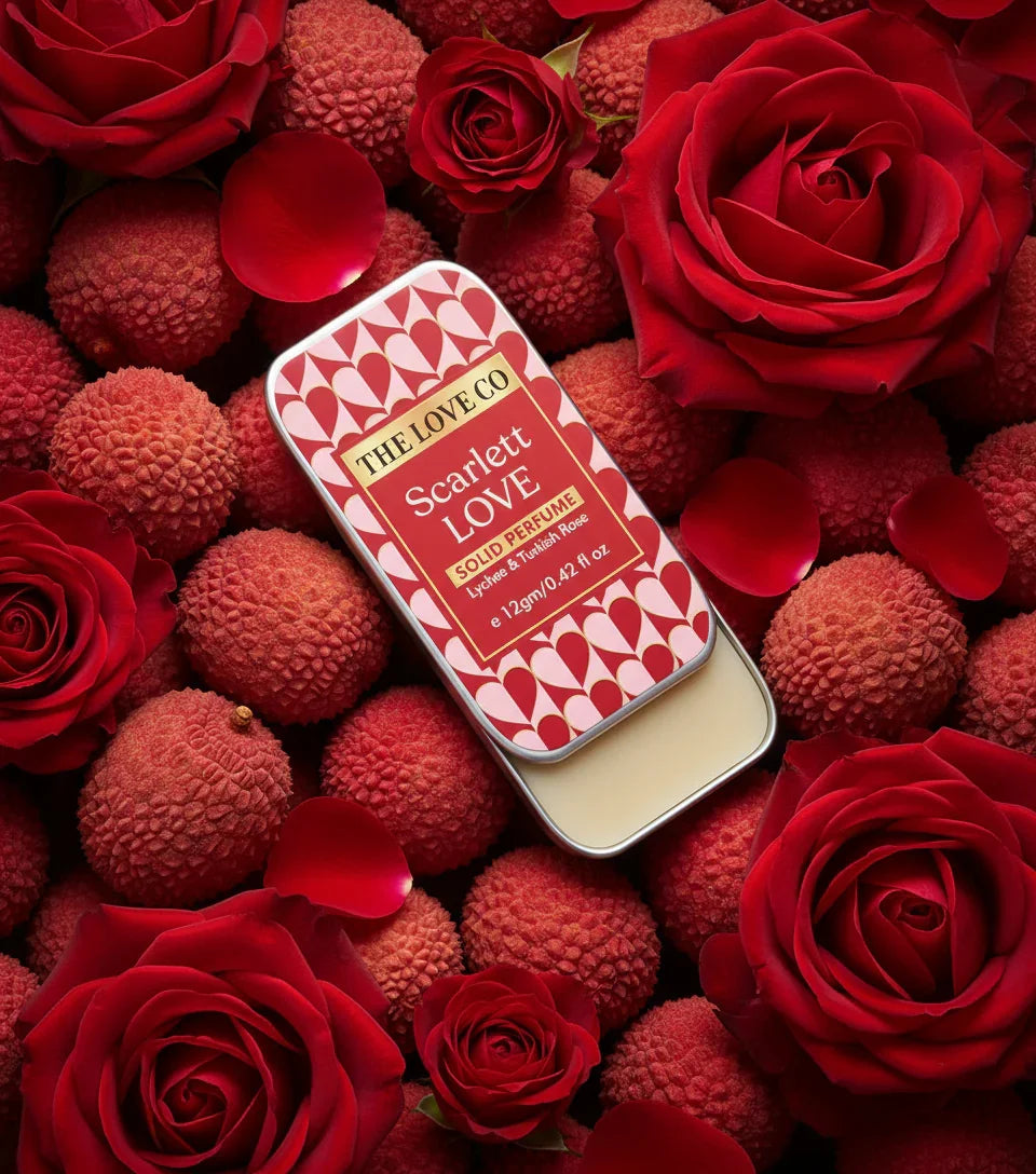 Scarlett Love solid perfume tin by The Love Co with lychee and roses, surrounded by red roses and lychees.