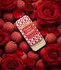 Scarlett Love solid perfume tin by The Love Co with lychee and roses, surrounded by red roses and lychees.