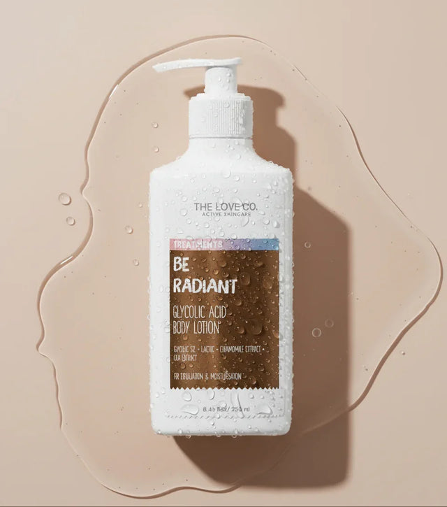The Love Co. Be Radiant Glycolic Acid Body Lotion bottle with water droplets on a beige background.