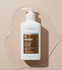 The Love Co. Be Radiant Glycolic Acid Body Lotion bottle with water droplets on a beige background.