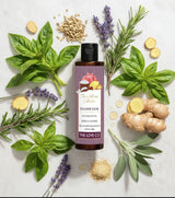 The Love Co hair oil bottle with herbs like basil, ginger, lavender, and rosemary on a light background