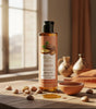 The Love Co argan oil bottle on wooden table with argan nuts and clay bowl in sunlight