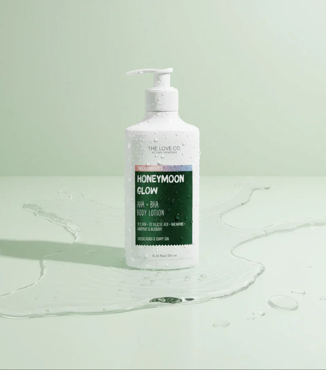 The Love Co Honeymoon Glow body lotion bottle with water drops on a light green background