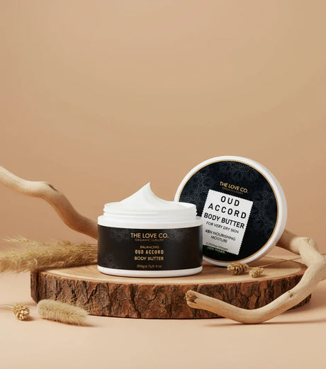 The Love Co Oud Accord Body Butter jar on wood with natural decor, black label visible