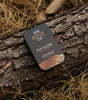 The Love Co Oud Accord solid perfume tin on tree bark with dried grass background