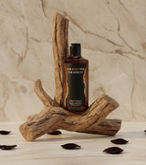 The Love Co Oud Black Rose body lotion bottle on rustic wood with rose petals, marble background