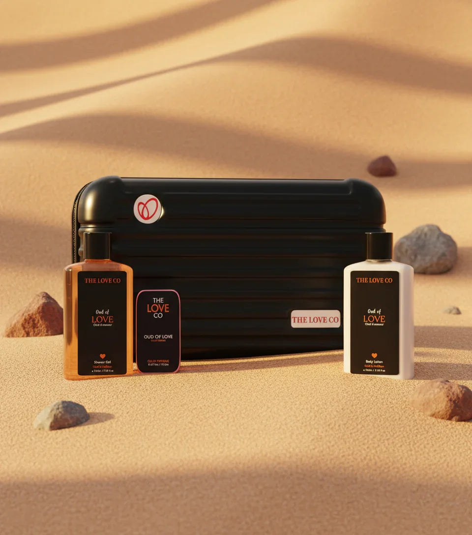 The Love Co Oud gift box with shower gel, body lotion, and perfume on desert sand.