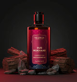 The Love Co. Oud Mukhaab shower gel bottle with oud wood and rocks on a dark background.