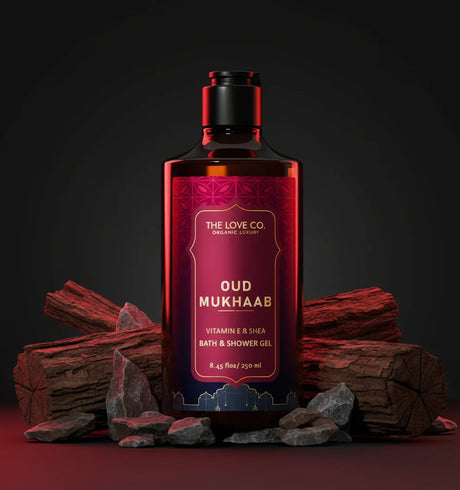 The Love Co. Oud Mukhaab shower gel bottle with oud wood and rocks on a dark background.