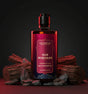 The Love Co. Oud Mukhaab shower gel bottle with oud wood and rocks on a dark background.