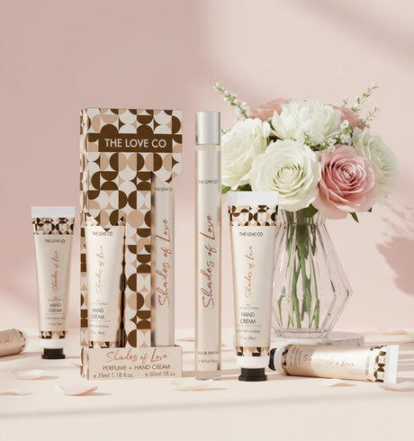 The Love Co Shades of Love gift set with perfume, hand cream, and flowers on a pink background.