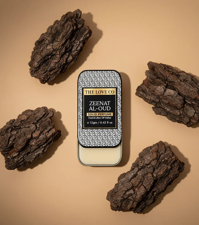 The Love Co Zeenat Al-Oud solid perfume tin with oud wood pieces on a beige background